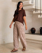 Woman wearing a brown top and patterned pants standing in a modern interior setting.