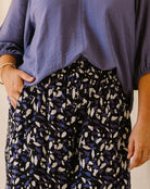 A close-up of a person wearing loose black pants with a blue and white abstract leaf pattern, paired with a lavender blouse.