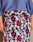 A close-up of a person wearing a black skirt with a dense multicolor floral print in pink, purple, white, and light green, paired with a blue blouse.