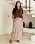 Woman wearing a brown t-shirt with a star design and a long patterned skirt in a modern indoor setting.