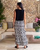 Woman in a black top and patterned skirt standing in a modern living room with stone wall and decorative elements.