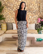 Woman in black top and patterned pants standing in a modern living room.