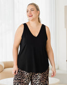 Woman wearing a black sleeveless top and leopard print pants indoors.