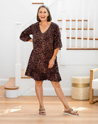 Woman in a brown patterned dress standing in a home interior.
