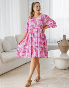 Woman wearing a pink and white patterned dress in a living room.