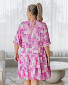 Woman wearing a pink and white patterned dress in a bright room.