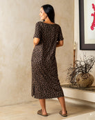 Woman wearing a leopard print dress standing in a room with a decorative vase and plant.