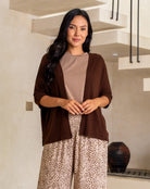 Woman wearing a brown cardigan, beige top, and leopard print pants standing in a modern interior setting.