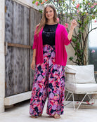 Woman wearing a pink cardigan and floral pants standing outdoors.