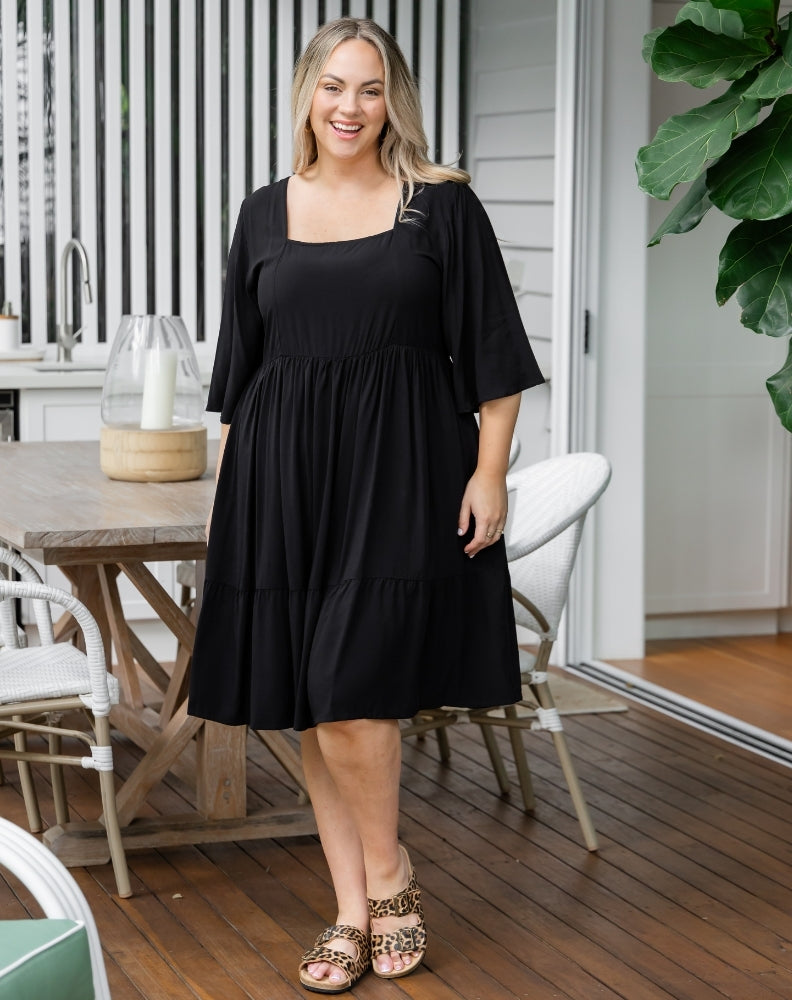 Woman in a black dress standing on a wooden deck with outdoor furniture in the background