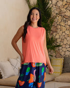 Woman wearing a coral sleeveless top and colorful skirt standing in a living room.