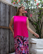 Woman wearing a bright pink sleeveless top and floral pants standing outdoors.
