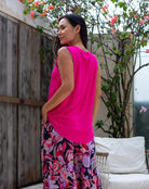 Woman wearing a bright pink sleeveless top and floral pants standing outdoors.