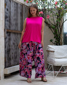 Woman wearing a bright pink top and floral pants standing in an outdoor setting.