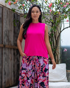 Woman wearing a bright pink top and floral skirt standing outdoors.