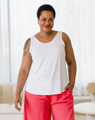 Woman wearing a white tank top and red pants standing in a room with light-colored walls and furniture.