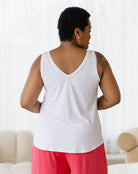 Person wearing a white tank top and pink pants in a room with a white couch and light-colored walls.