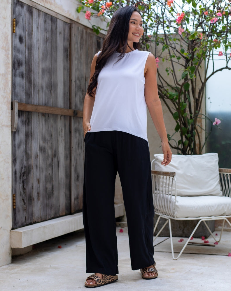 Woman wearing a white sleeveless top and black pants standing outdoors.