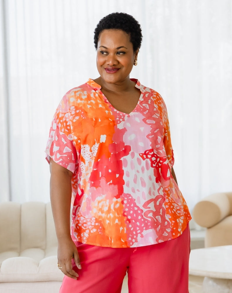 Woman wearing a colorful blouse and pink pants in a living room setting