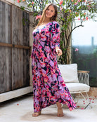 Woman in a floral dress standing outdoors with a wooden fence and chair in the background