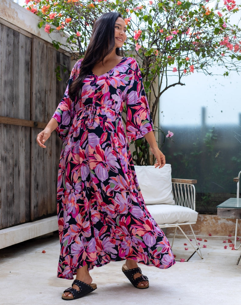 Woman in a floral dress standing outdoors with a wooden fence and tree in the background